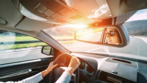 a person driving down the road with both hands on the wheel and their smiling face reflected in the rearview mirror