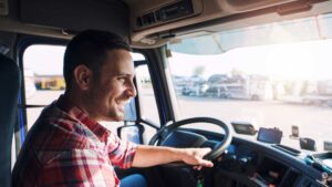 a truck driver behind the wheel and smiling in the sunshine