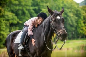 Child girl rides horse on the outdoors in the middle of the forest, park, trees, mountains.